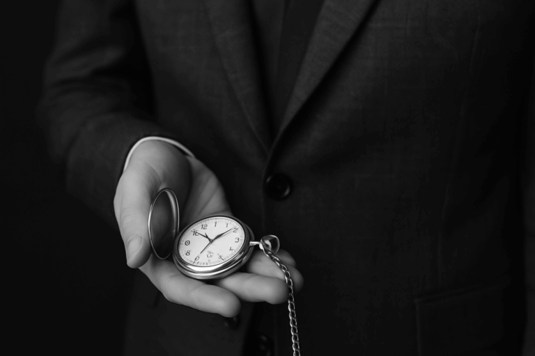 Black and white photo of a man in a dark suit holding a white gold pocket watch with a chain in his hand