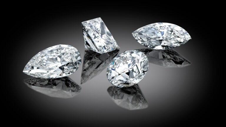 Four loose diamonds in round, marquise, pear, and princess cuts displayed on a reflective black background